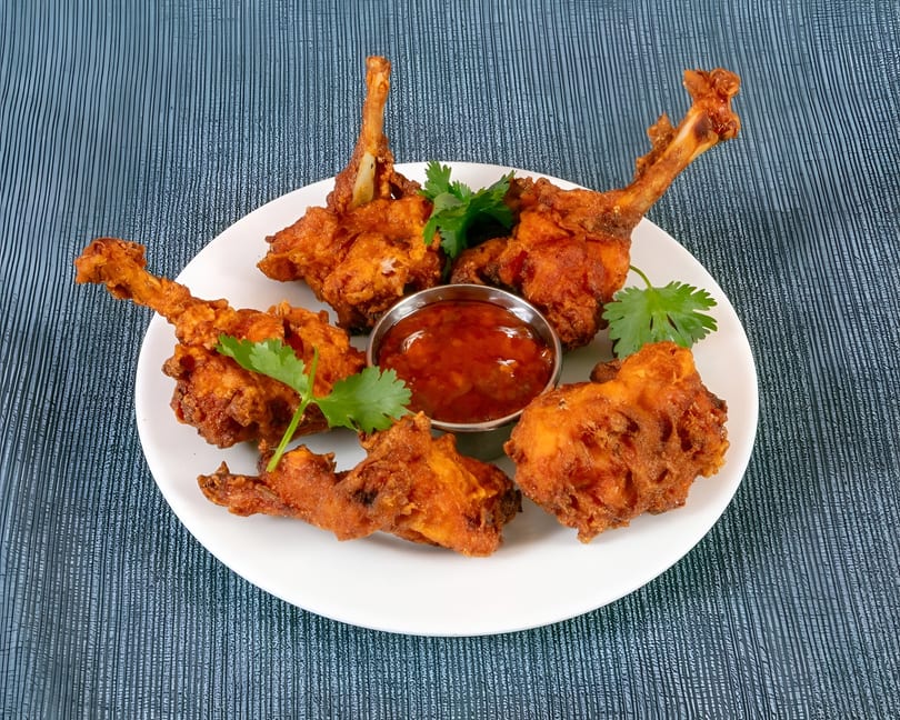 Crispy fried chicken lollipops with fresh cilantro and sweet chili dipping sauce on a white plate.