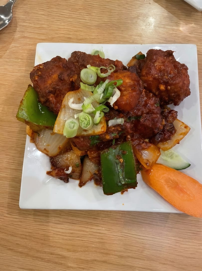 Spicy chicken dish with green peppers, onions, and scallions on a white rectangular plate.