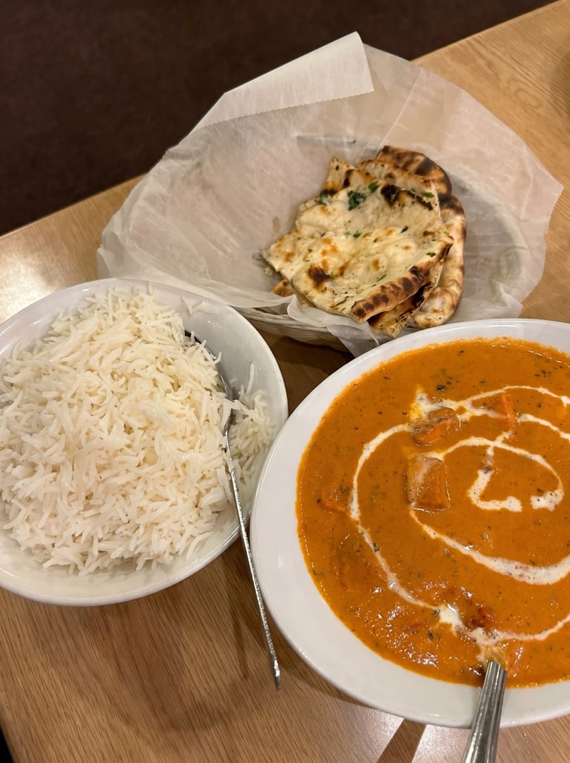 Indian meal with butter chicken, basmati rice, and naan bread on a wooden table.