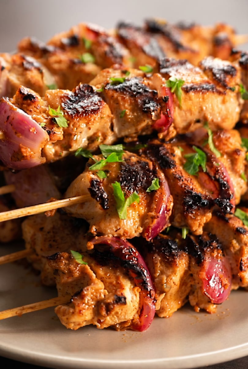 Close-up of grilled chicken and red onion skewers, garnished with fresh parsley on a gray plate.