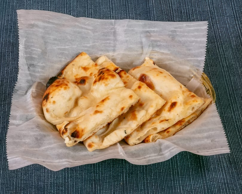 Golden-brown naan bread pieces, some with charred spots, served in a basket lined with white paper.