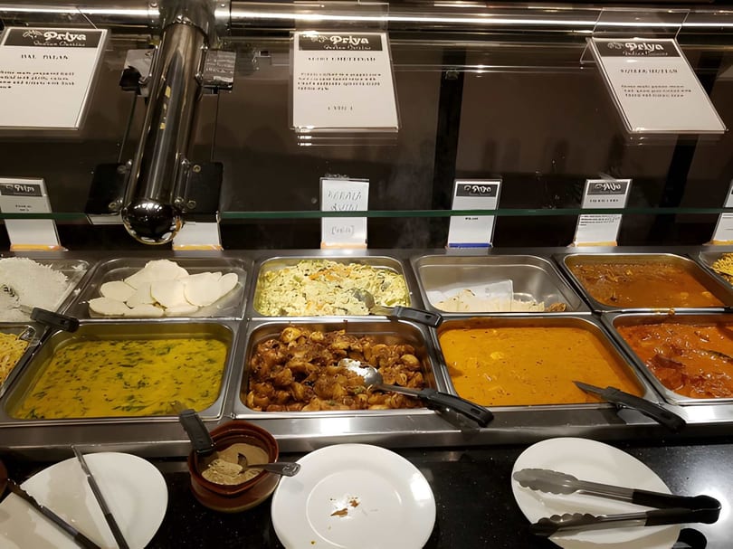 A buffet spread at Priya Indian Cuisine with various dishes in metal trays and serving utensils.