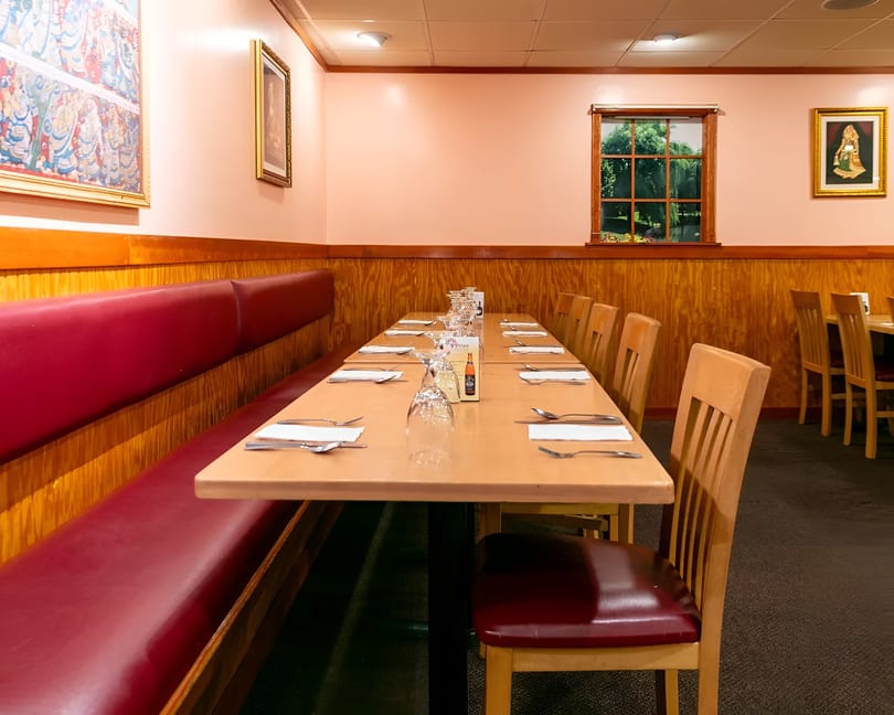 A long dining table set with silverware and glasses, flanked by a red booth and wooden chairs.