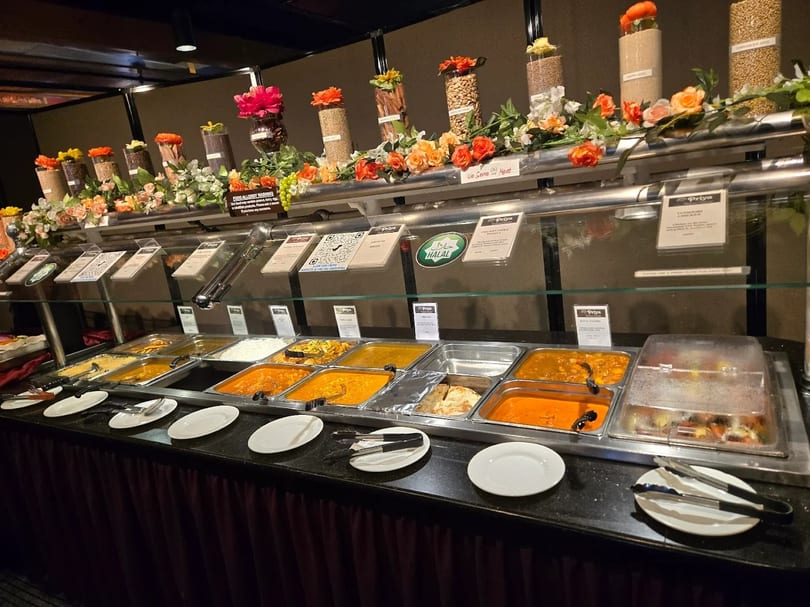 A long buffet table at Priya Indian Cuisine, filled with various dishes in metal trays.