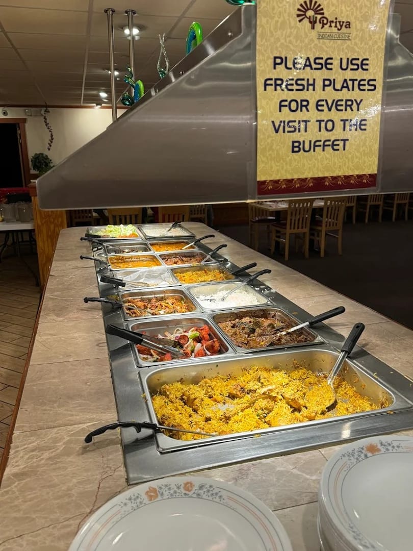 Priya Indian Cuisine buffet line with various dishes, fresh plates, and a sign for new plates.