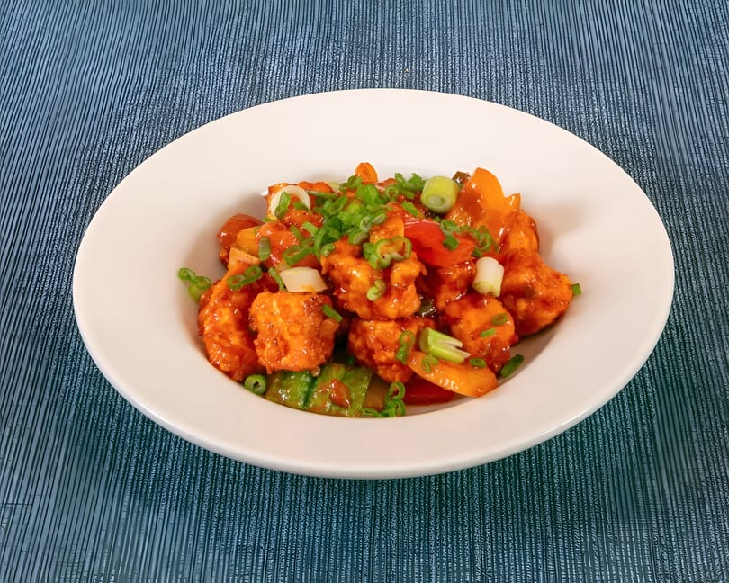 Sweet and sour chicken with bell peppers and green onions in a white bowl.